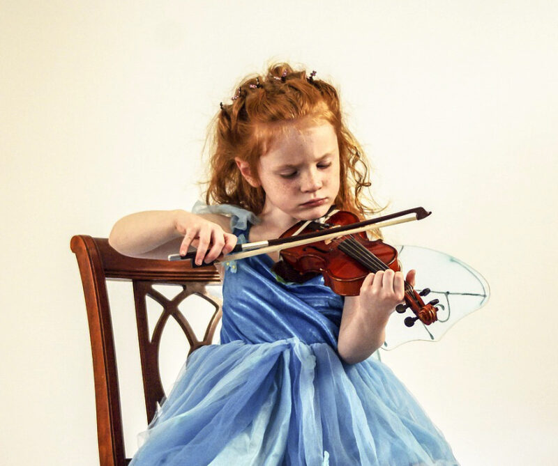 椅子に座ってバイオリンを弾く青いドレスの少女の画像